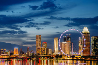 Illuminated ferris wheel in city against sky