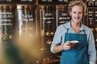Portrait of smiling coffee roaster in his shop drinking cup of coffee