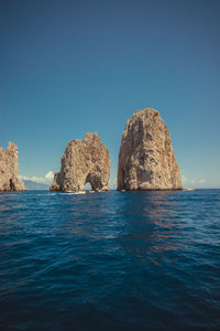 Rocks in sea against clear blue sky