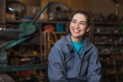Smiling manual worker looking away while sitting in workshop