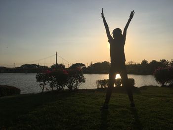 Silhouette person standing at riverbank against sky during sunset