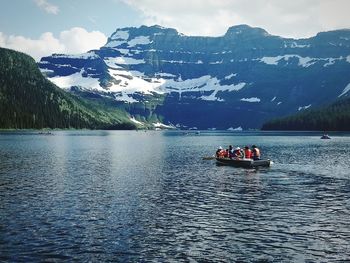 People sitting in boat on lake against mountains