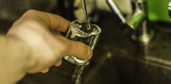 Cropped hand of person filling water in shot glass