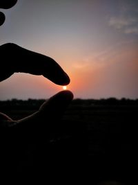 Silhouette person holding sun against sky during sunset