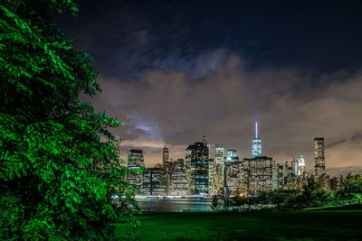 Grassy field against illuminated buildings and sky in park at night