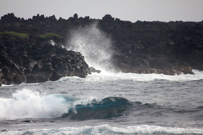 Waves splashing on rocks against clear sky