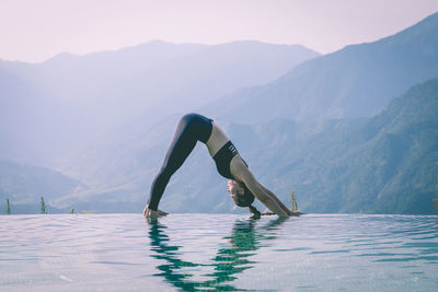 Side view full length of woman exercising against mountains at infinity pool