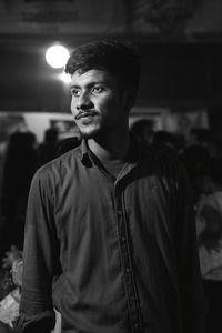 Young man looking away against illuminated lights