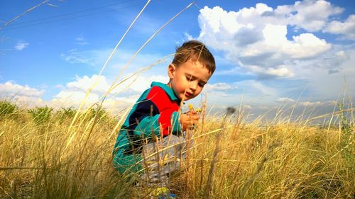 Boy crouching on grassy field against sky