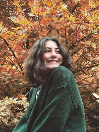 Low angle view of smiling young woman against trees during autumn