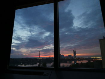 Silhouette buildings against sky seen through glass window