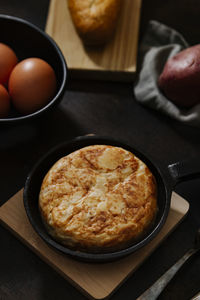 Spanish potato omelette with some fresh eggs shot from high angle over a wooden surface in a dark still life picture. vertical image.
