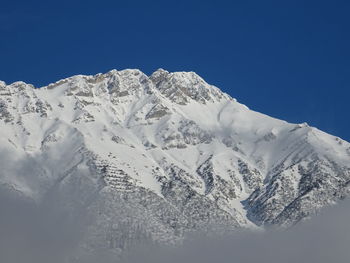 Low angle view of snowcapped mountains against clear blue sky