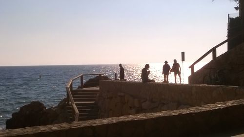 People standing on railing by sea against clear sky