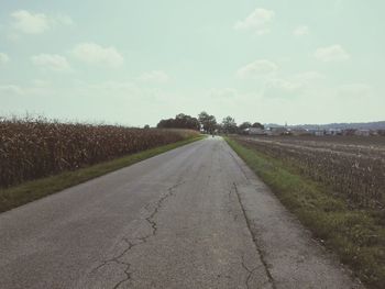 Empty road amidst field against sky