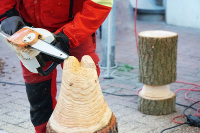 Midsection of worker sawing wood with chainsaw
