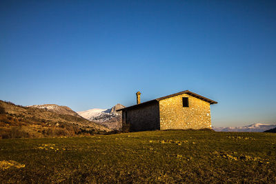 Building on field against clear blue sky