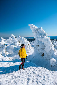 Rear view of man standing on snowcapped mountain against blue sky