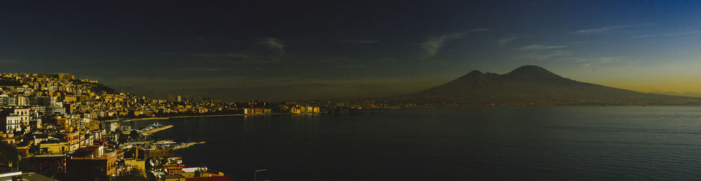 Illuminated city by sea against sky at night