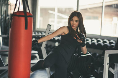 Confident young woman kicking punching bag in gym