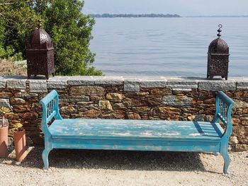 Empty bench by sea against sky