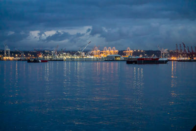 Sea by illuminated city against sky at night