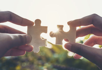 Cropped image of hands holding jigsaw puzzle against sky