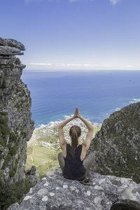 Man standing on rock by sea against sky