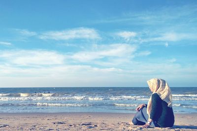 Woman sitting at beach against sky