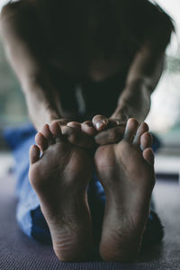 Low section of woman stretching while sitting on floor at home