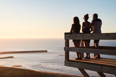 Rear view of people sitting on beach during sunset