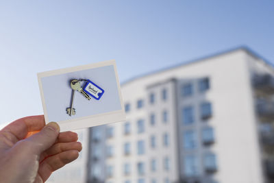 Hand holding photo of keys in front of building