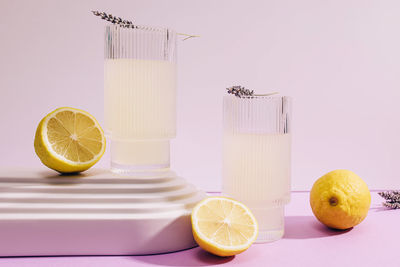 Lavender lemonade in ribbed glasses and lemons on purple background, direct sunlight effect