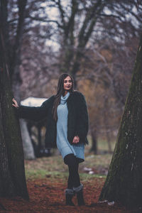 Woman standing by tree trunk in forest