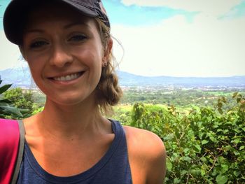 Portrait of smiling young woman standing on field against sky