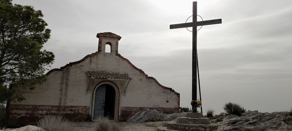 Low angle view of cross by building against sky