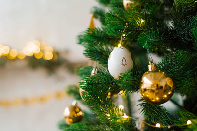 The christmas tree is decorated with toys, golden balls, white eggs and garlands in close-up