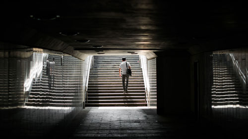 Rear view of man climbing on stairs at underground walkway