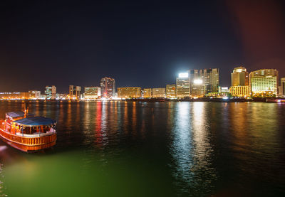 Illuminated buildings by river against sky at night