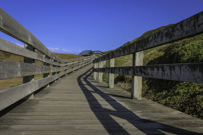 Empty footbridge against clear blue sky