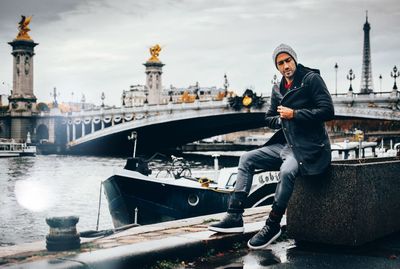 Man sitting at harbor in city against sky