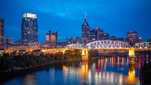 Illuminated buildings by river against sky at night