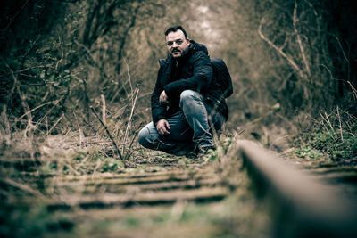 Full length portrait of young man sitting in forest