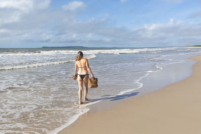 Woman in bikini walking on beach sand against blue sky. 