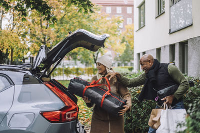 Man assisting woman loading luggage in car trunk while relocating house