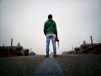 Rear view of man standing on street against clear sky