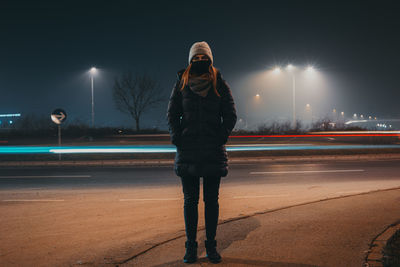 Full length of woman wearing mask standing on street at night