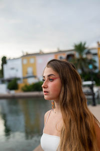 Tranquil young female with long hair standing on embankment in tropical city in summer evening