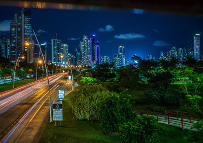 Light trails on street amidst buildings against sky at night