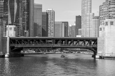Bridge over river by buildings in city against sky